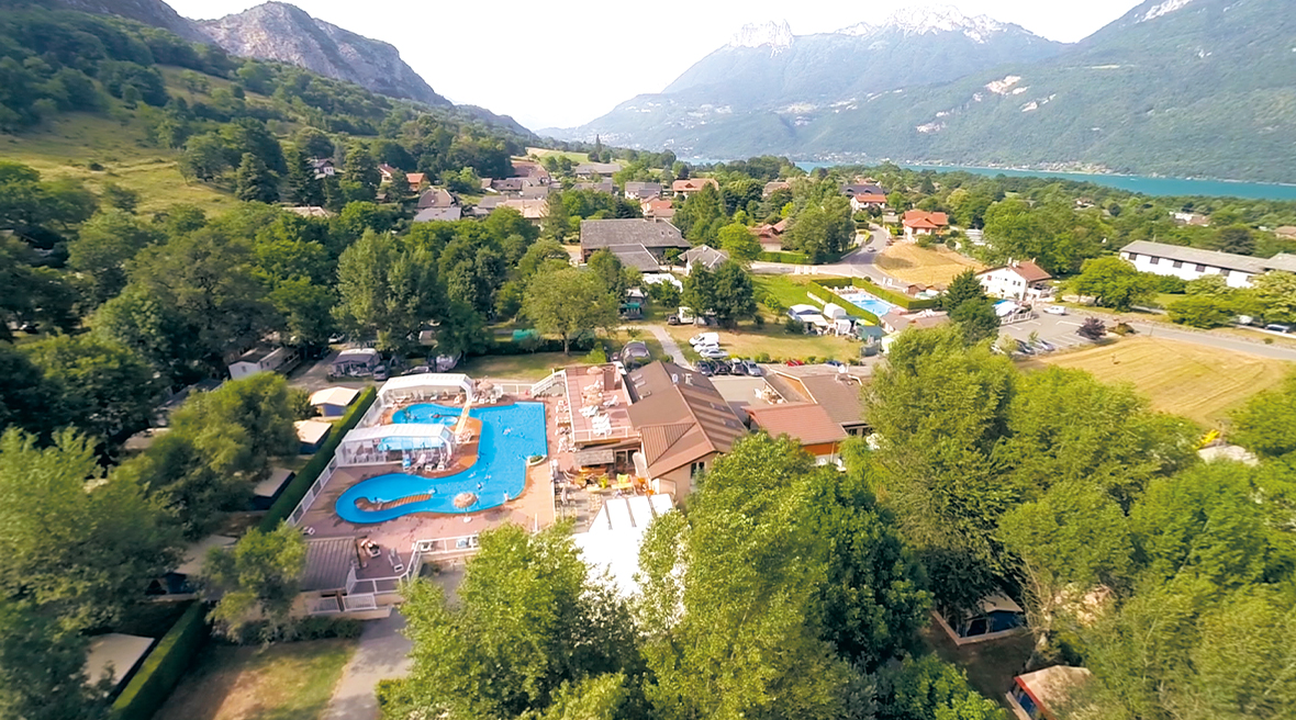 Swimming pool and lush forestry with a lake and snow-capped mountains in the background
